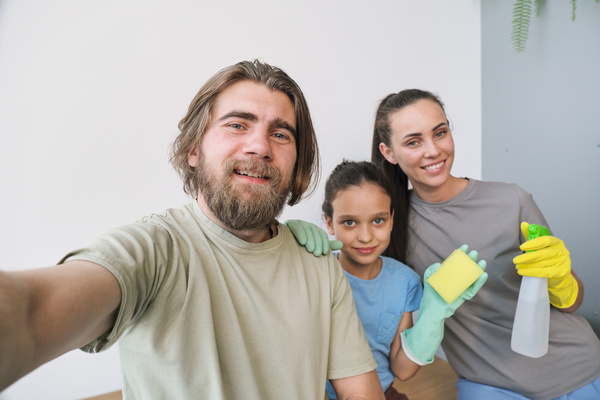 Selfie of a man with his wife and daughter in multi-colored rubber gloves with cleaning equipment in the form of a sponge and a sprayer