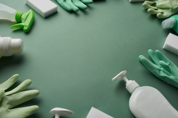 A general cleaning set of detergents melamine sponges and rubber gloves is laid out in a circle on a green surface