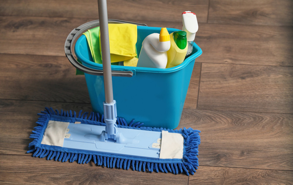 A floor cleaning set consisting of a mop and a blue bucket with household chemicals is on the parquet