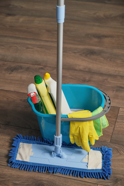 A set for washing the floor consisting of a bucket with cleaning agents rubber gloves and a mop with a microfiber nozzle on the parquet
