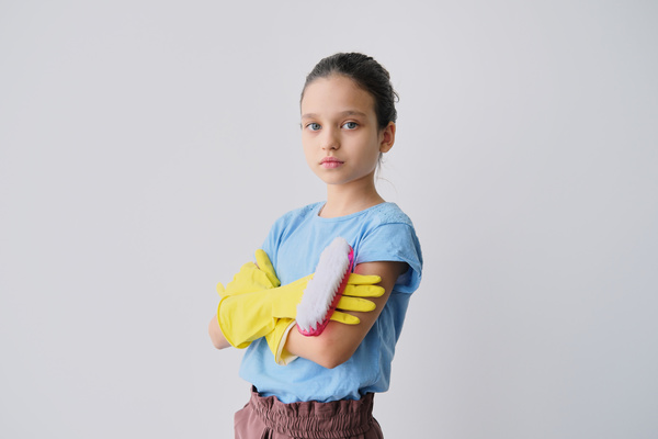 A girl with her hair in a bun and wearing yellow rubber gloves with her arms crossed on her chest holds a red brush-iron