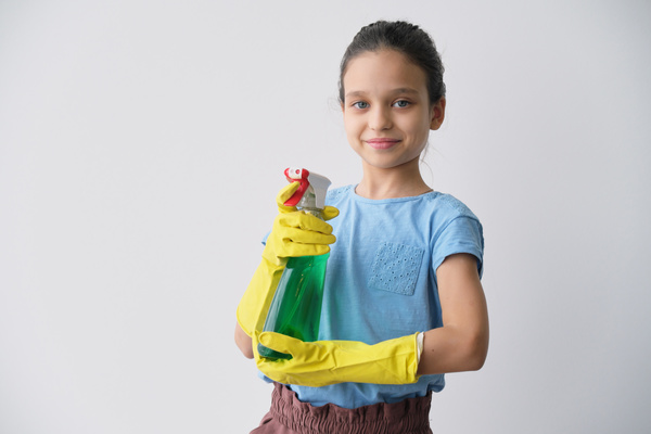 A girl in yellow rubber gloves smiling with a green cleaning agent in a spray bottle in hands