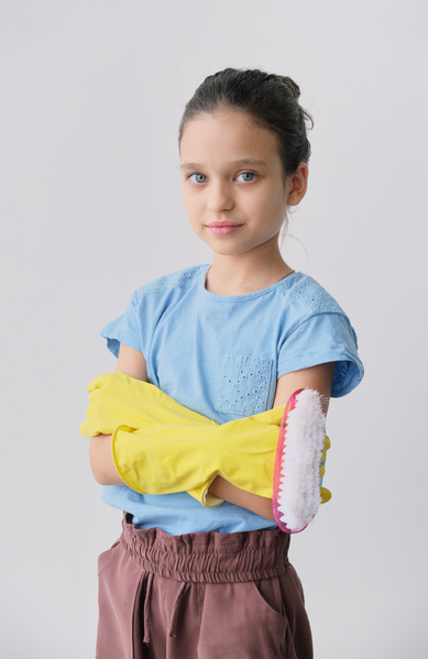 A girl with yellow rubber gloves on her hands holding an iron brush with her arms crossed on her chest
