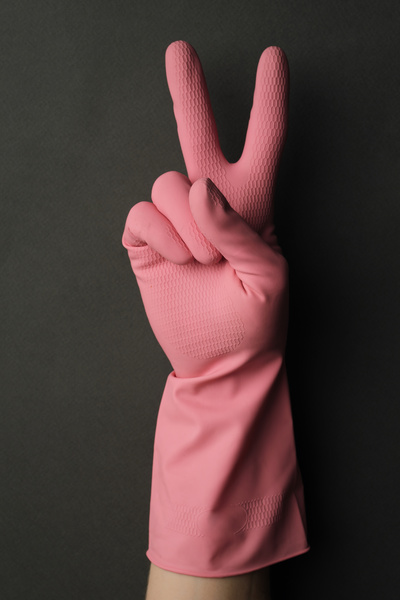 A peace sign shown by a hand in a pink rubber glove on a dark background