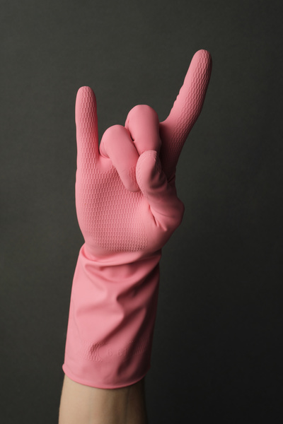 The goat gesture shown by a hand in a pink rubber glove on a dark background