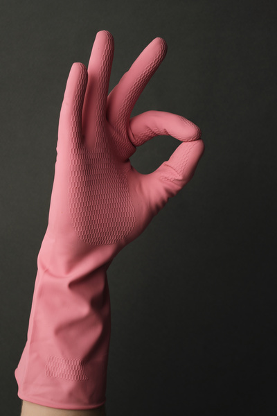 A man shows a sign of consent with his hand in a pink rubber glove on a dark background