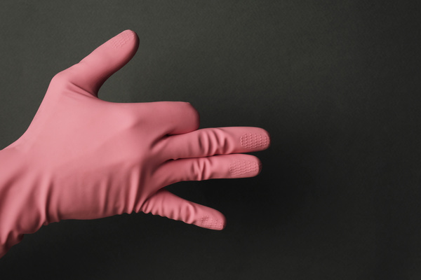 A man shows the figure of a wolf with his hand in a pink rubber glove on a dark background