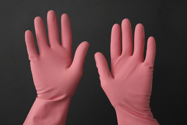 Hands in pink rubber gloves with a ribbed surface on a dark background