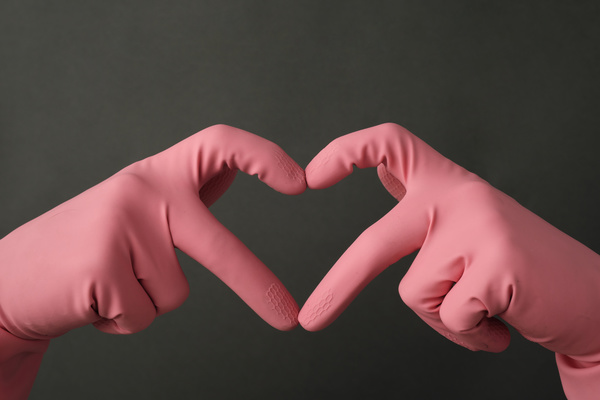 The heart is folded with hands in pink rubber gloves with a ribbed surface on a dark background