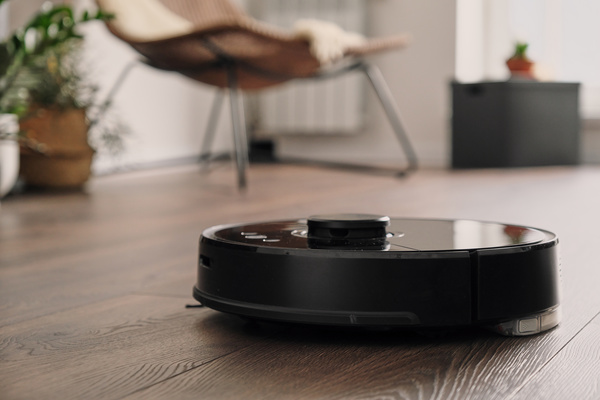A black robot vacuum hoovering the dark wooden parquet in the living room