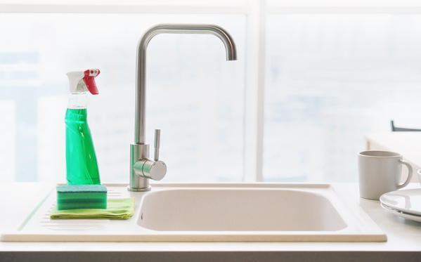Kitchen sink and green cleaning agent in a spray bottle with a sponge for washing dishes and a cleaning cloth