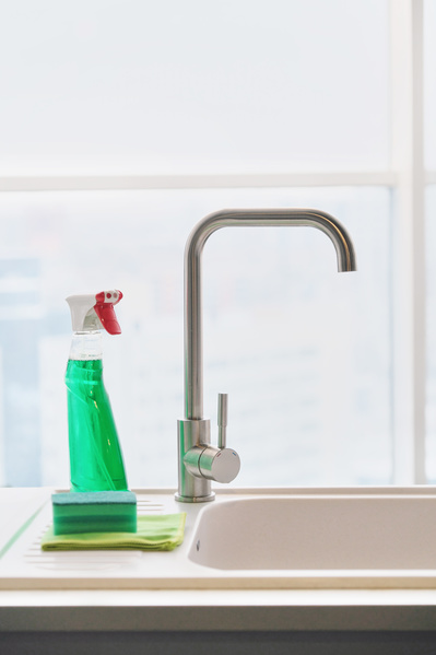 Kitchen metal faucet and green detergent in a sprayer with a sponge for washing dishes and a cleaning cloth