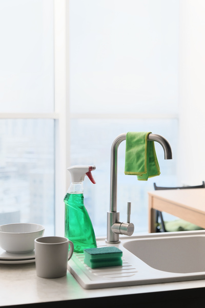 A cleaning cloth on the kitchen faucet and detergent in a spray bottle with dishes nearby