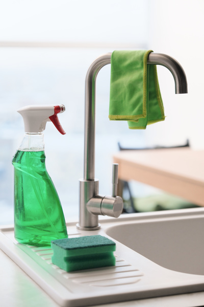 Microfiber for cleaning on the kitchen faucet and household chemicals in a spray bottle with a sponge next to it