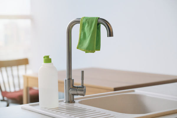 A cleaning rag on the kitchen faucet and household chemicals in a bottle with a sponge next to it