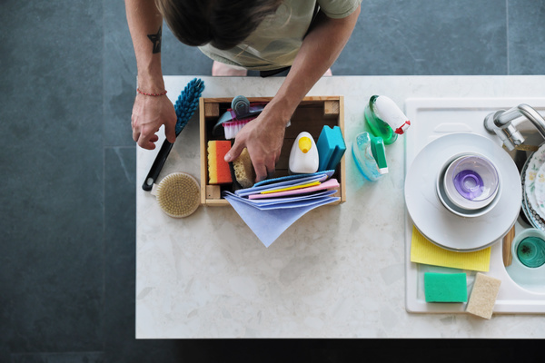 A man puts a sponge for washing dishes and a cleaning brush in a wooden box with a cleaning kit