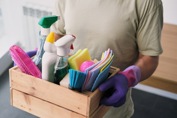 A man holds a wooden box with a cleaning kit consisting of household chemicals and cleaning equipment