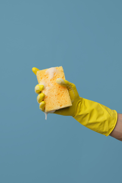 Yellow foam sponge for washing dishes in the hand in a yellow rubber glove on a blue background