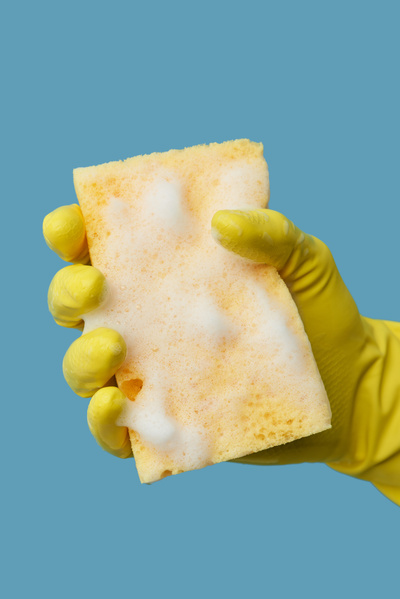 A yellow soap sponge for washing dishes is held in the hand in a yellow rubber glove on a blue background