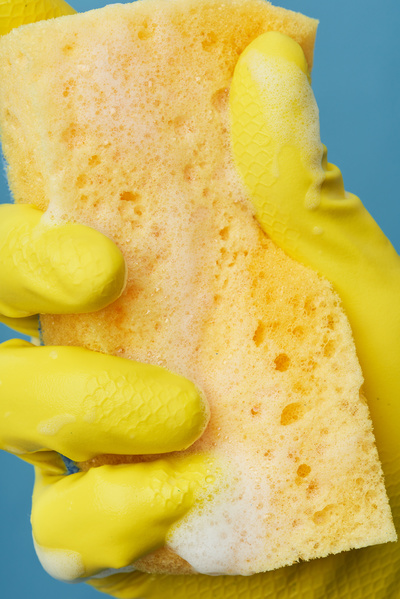 A hand in a yellow rubber glove with a foam sponge for washing dishes on a blue background