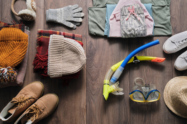 piles of clothes of different seasons and swimming accessories are laid out on the dark wood floor