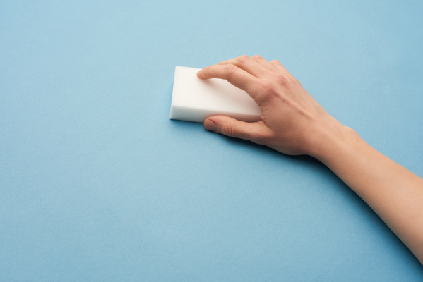 White melamine cleaning sponge is in the hand on a blue background