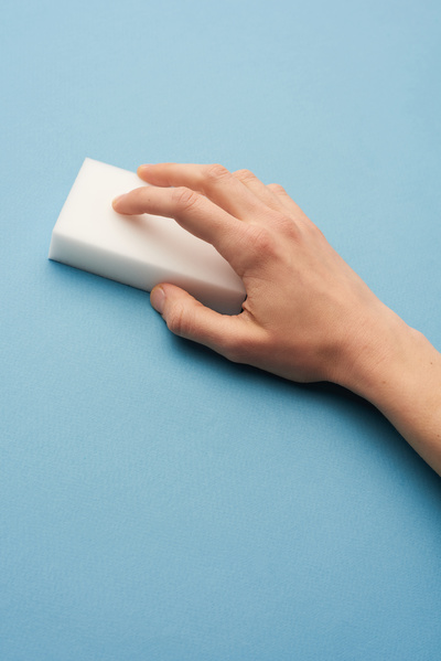 A white melamine sponge for washing is in the hand on a blue background