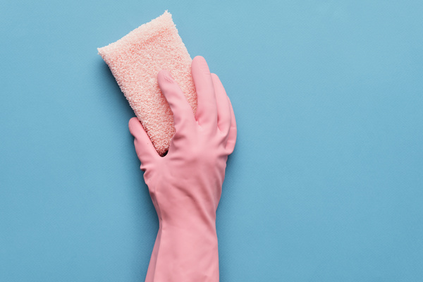 A pink terry sponge is in the hand in a pink rubber glove on a blue background