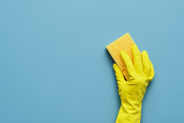 A yellow sponge for washing dishes is held with a hand in a yellow rubber glove on a blue background