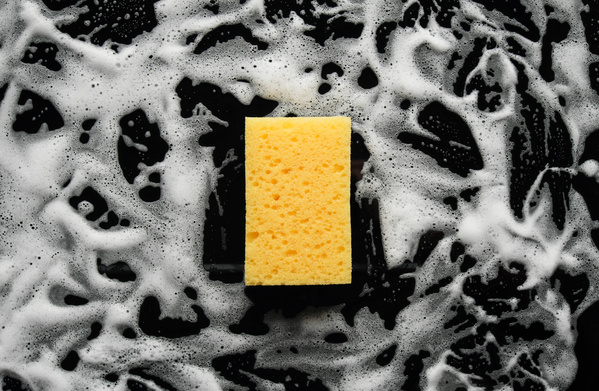 Yellow sponge for washing dishes on a black surface in foam