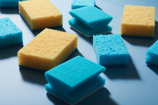 Blue and yellow sponges for washing are randomly laid out on a blue surface