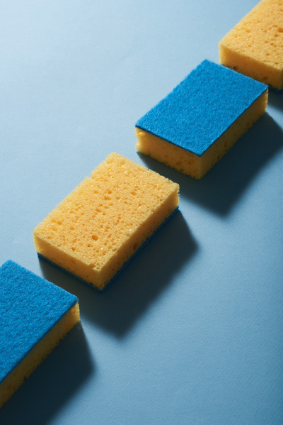 Sponges for washing dishes of blue yellow color laid out in a row on a blue surface cast a shadow