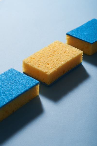 Blue yellow cleaning sponges laid out in a row on a blue surface cast a shadow