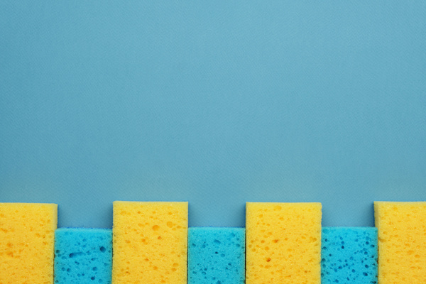 A flatlay of blue-yellow cleaning sponges lying tightly in a row on a blue surface
