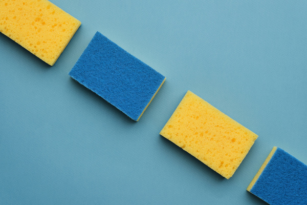 A flatlay of blue and yellow sponges for washing dishes lie in a row on a blue surface