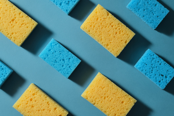 A flatlay of blue and yellow cleaning sponges laid out in a checkerboard pattern on a blue surface