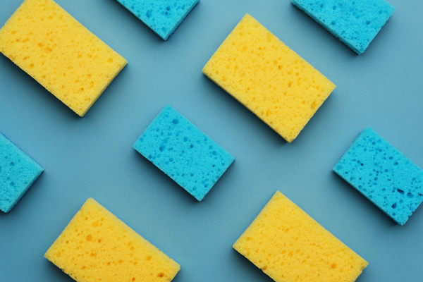 A flatlay of blue-yellow scrubbing sponges laid out in a checkerboard pattern on a blue surface