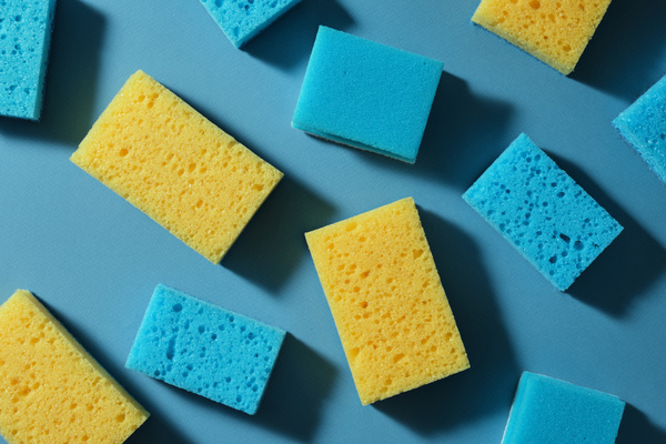 A flatlay of blue-yellow sponges for washing and melanin sponges scattered on a blue surface
