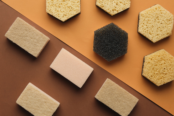 Sponges for cleaning different shapes of light color with a dark abrasive surface are laid out in order on the surface of brown shades