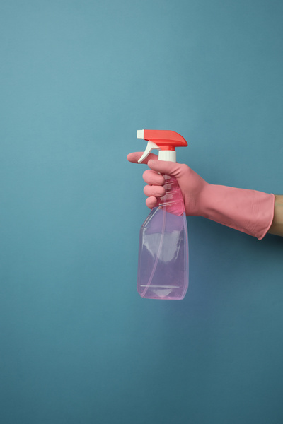 Household chemicals in the spray gun in a hand in a pink rubber glove on a blue background