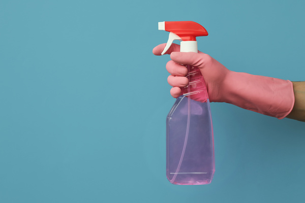 Detergent in the spray gun in the hand in a pink rubber glove on a blue background