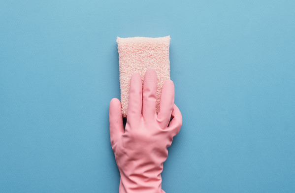 A soft pink terry sponge for cleaning is held in the hand in a pink rubber glove on a blue surface