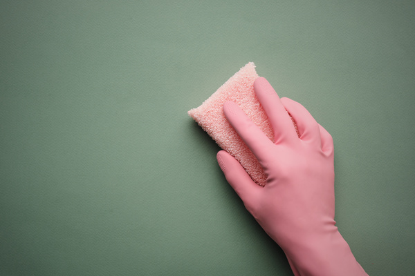 A hand in a pink rubber glove with a terry sponge for washing dishes on a dark green background