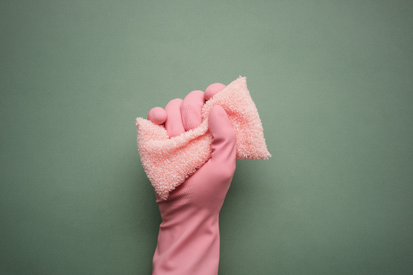 A hand in a pink rubber glove squeezing a terry sponge for washing dishes on a dark green background