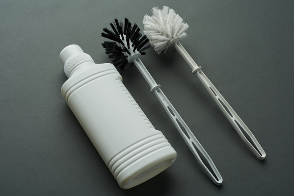 A bottle of household chemicals and toilet brushes in black and white on a dark matte surface