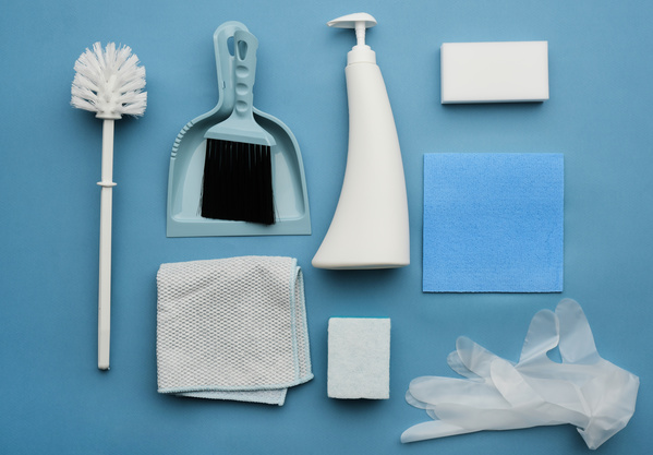 A toilet brush a dustpan and a floor brush melamine sponges gloves and cleaning cloths on a blue surface