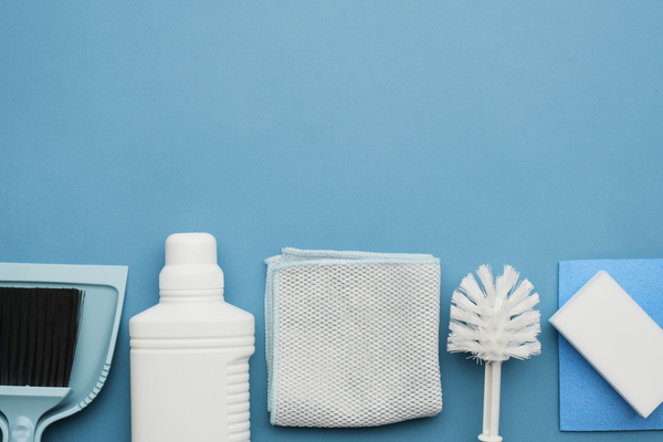 Pieces of cleaning equipment such as a dustpan and a floor brush household chemicals and cleaning cloths and melamine sponges lie in a row on a blue surface