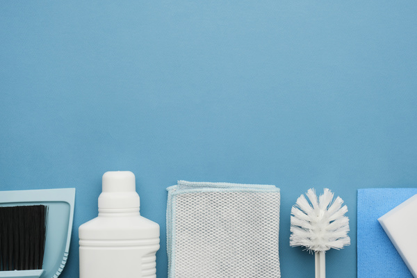 Cleaning tools such as a dustpan and a floor brush household chemicals and cleaning cloths and melamine sponges lie in a row on a blue surface