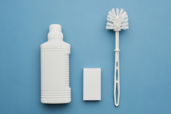 A white bottle with a cleaning agent melamine sponge and a toilet brush on a blue surface