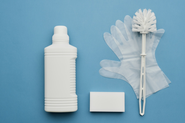 White bottle with detergent rubber gloves melamine sponge and toilet brush on a blue surface